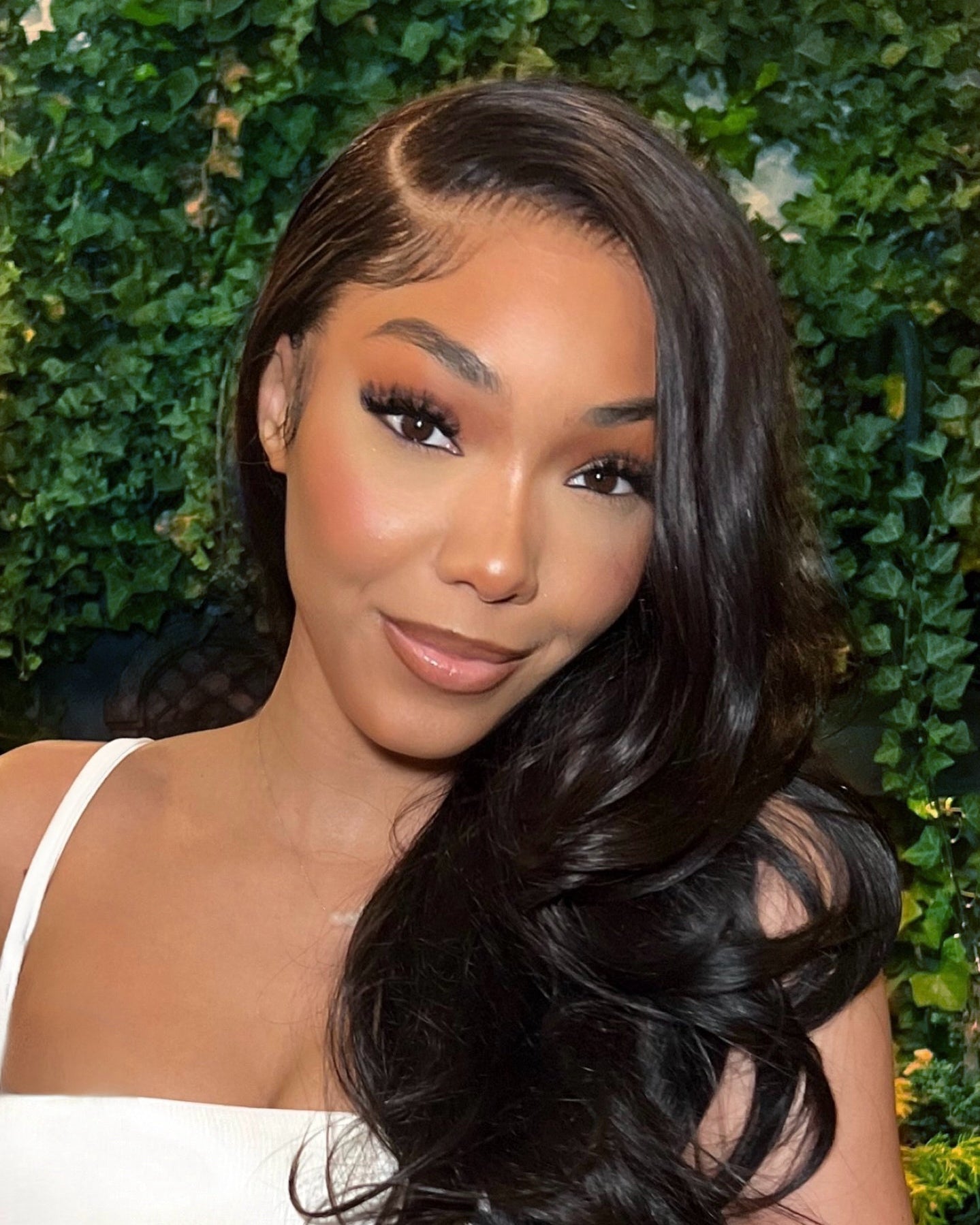 Woman with long, wavy hair against a green leafy background